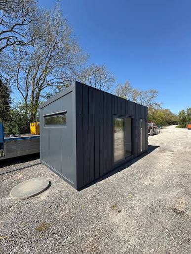 Dark grey modular building with vertical cladding, glazed doors and a narrow side window